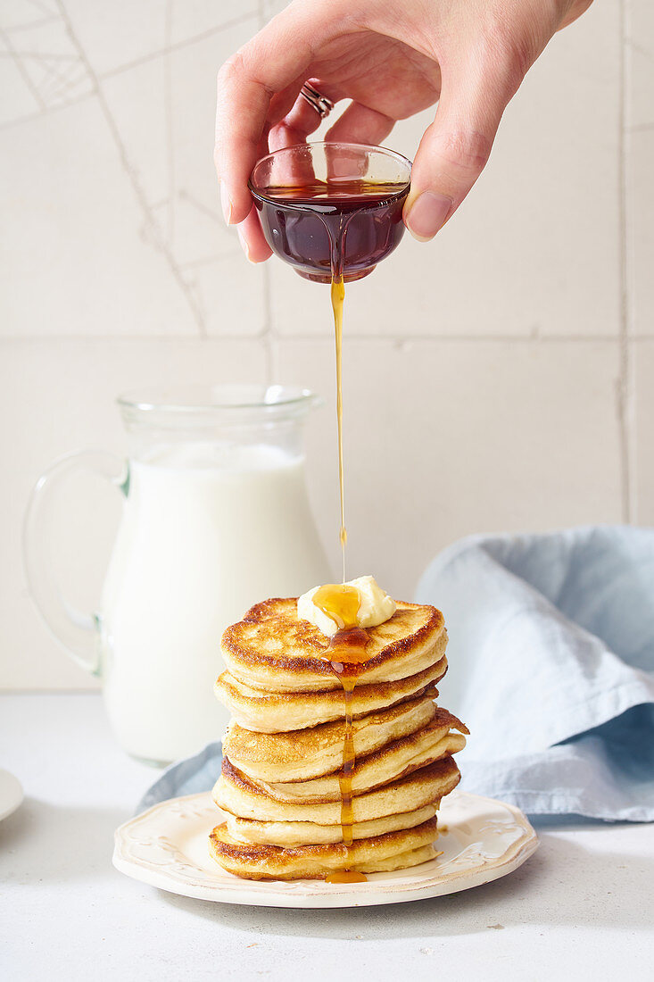 Pouring maple syrup on a stack of pancakes with butter