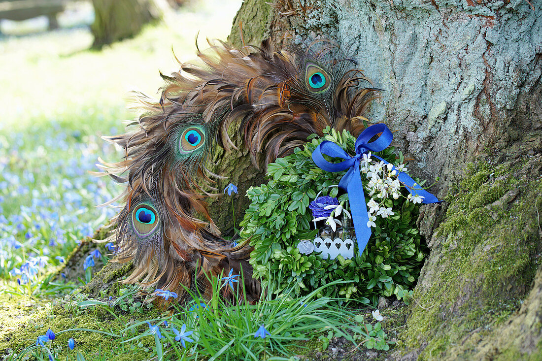 Buchskranz mit blauer Schleife und Blüten an Kranz aus Pfauenfedern