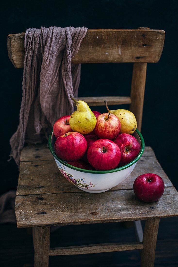 Äpfel und Birnen in Keramikschale auf Holzstuhl