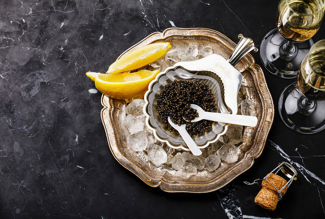 Black caviar in silver bowl and Champagne on black marble background copy space