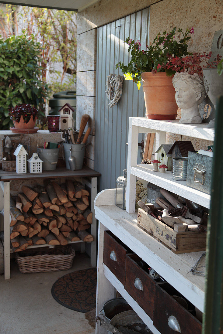 Regale mit Feuerholz, Gartenzubehör und Vintage-Deko an der Hauswand