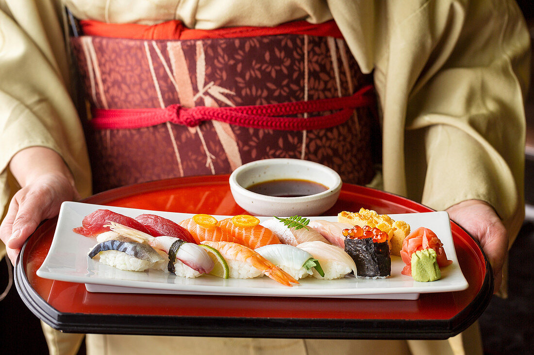 A woman wearing a kimono holding a tray of sushi