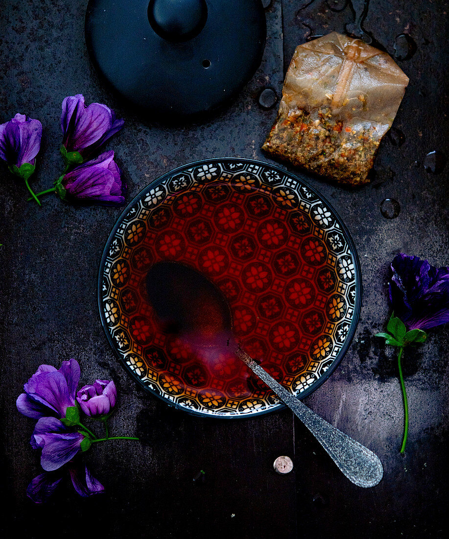 Brewed purple mallow tea in a bowl next to a teabag