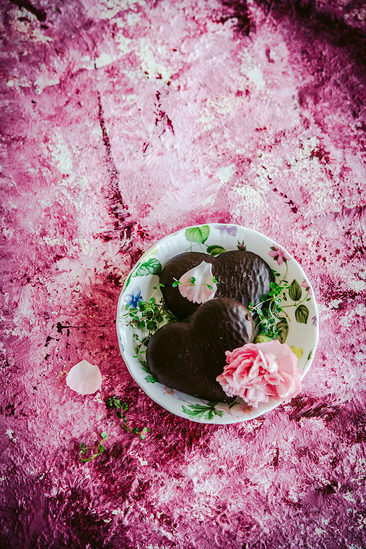 Schokoladenplätzchen mit rosa Nelkenblüte auf pinkfarbenem Untergrund