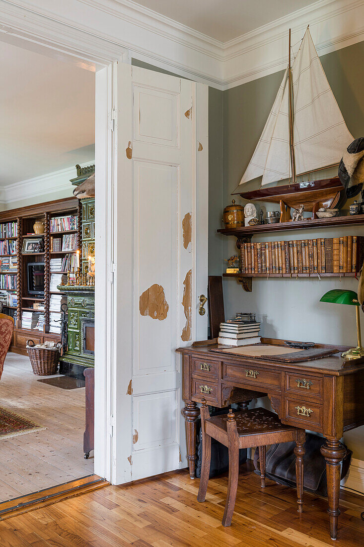 Antique desk below shelf with model sailboat in corner of room