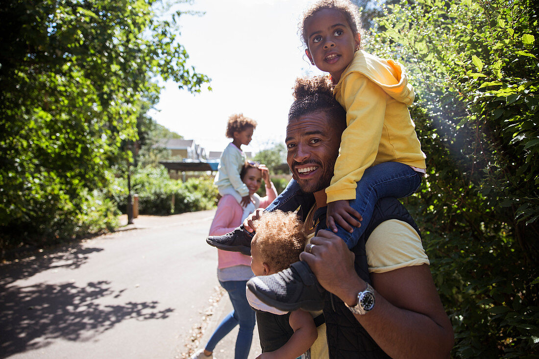 Portrait happy father carrying daughters on sidewalk