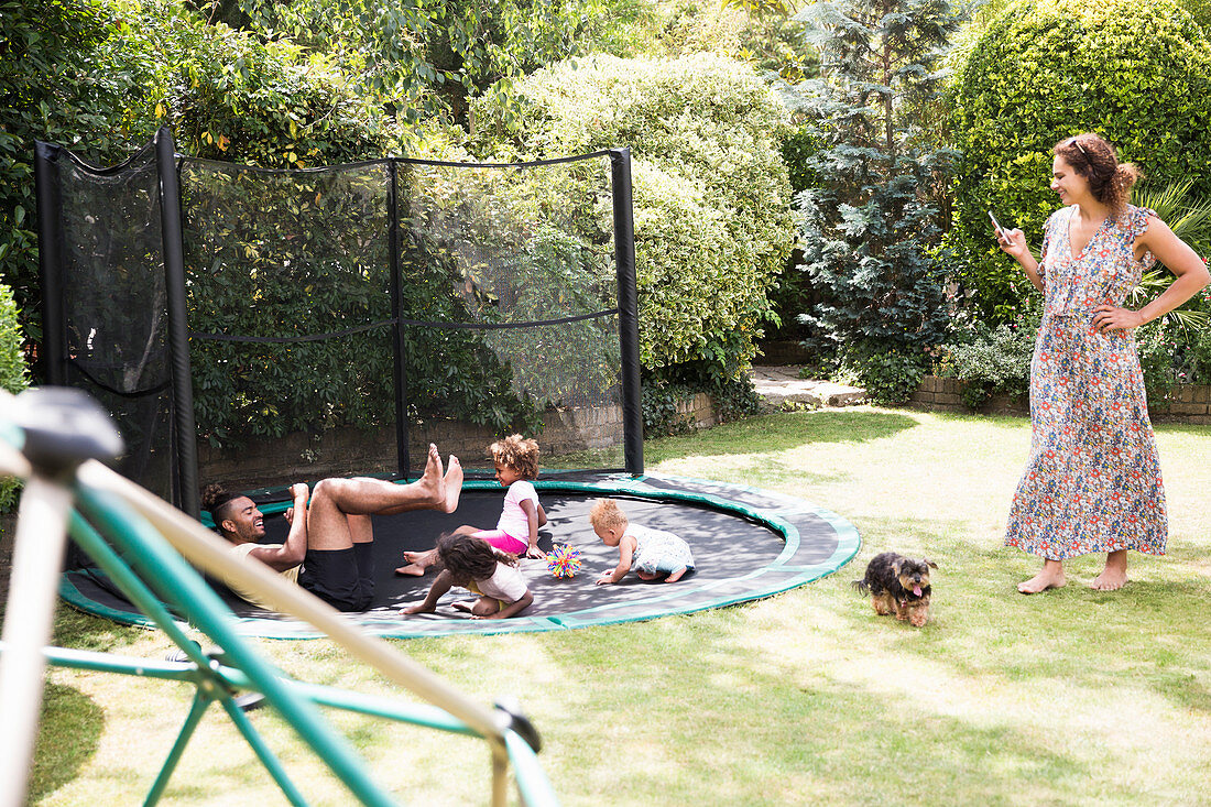 Family playing on sunny backyard trampoline