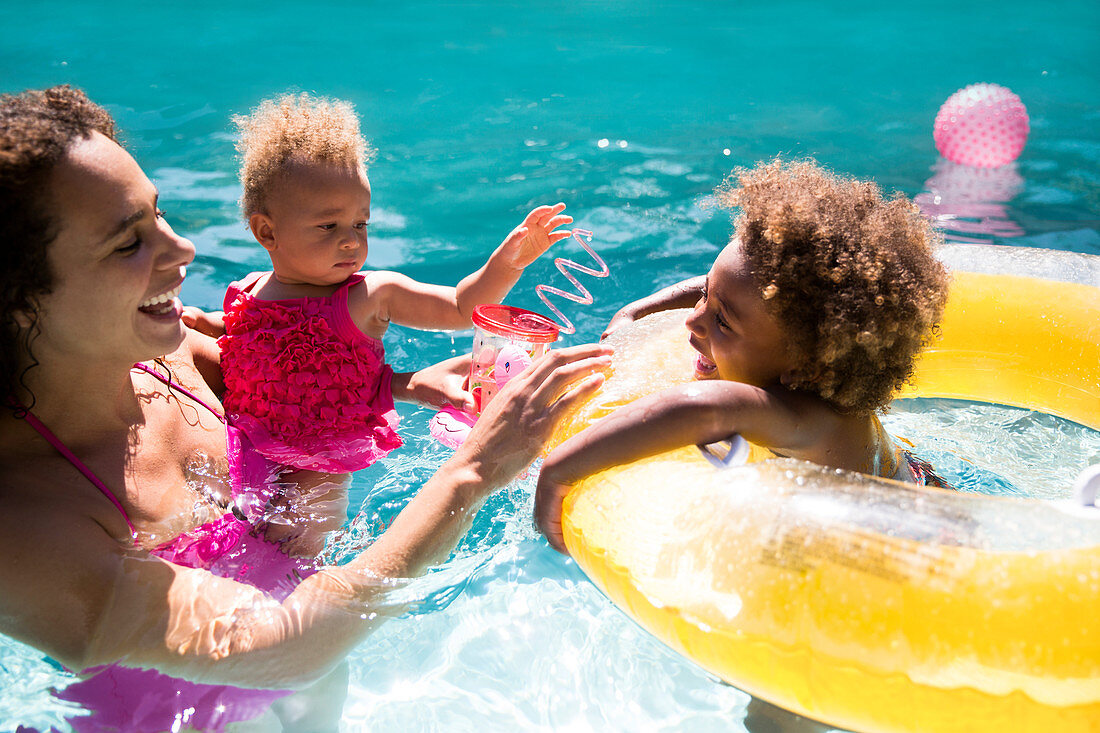 Mother and daughters playing in summer swimming pool