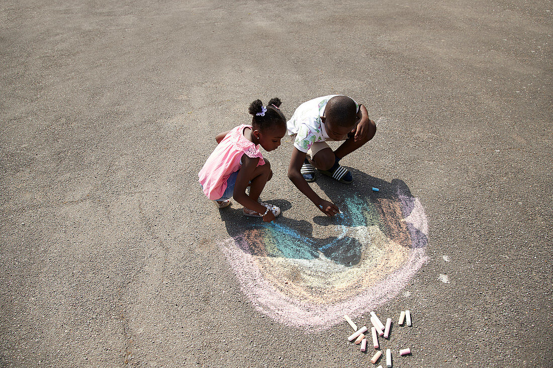 Brother and sister drawing rainbow on pavement