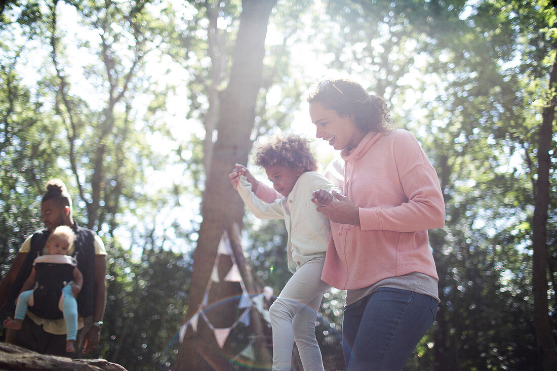 Mother helping daughter balance on fallen log in woods