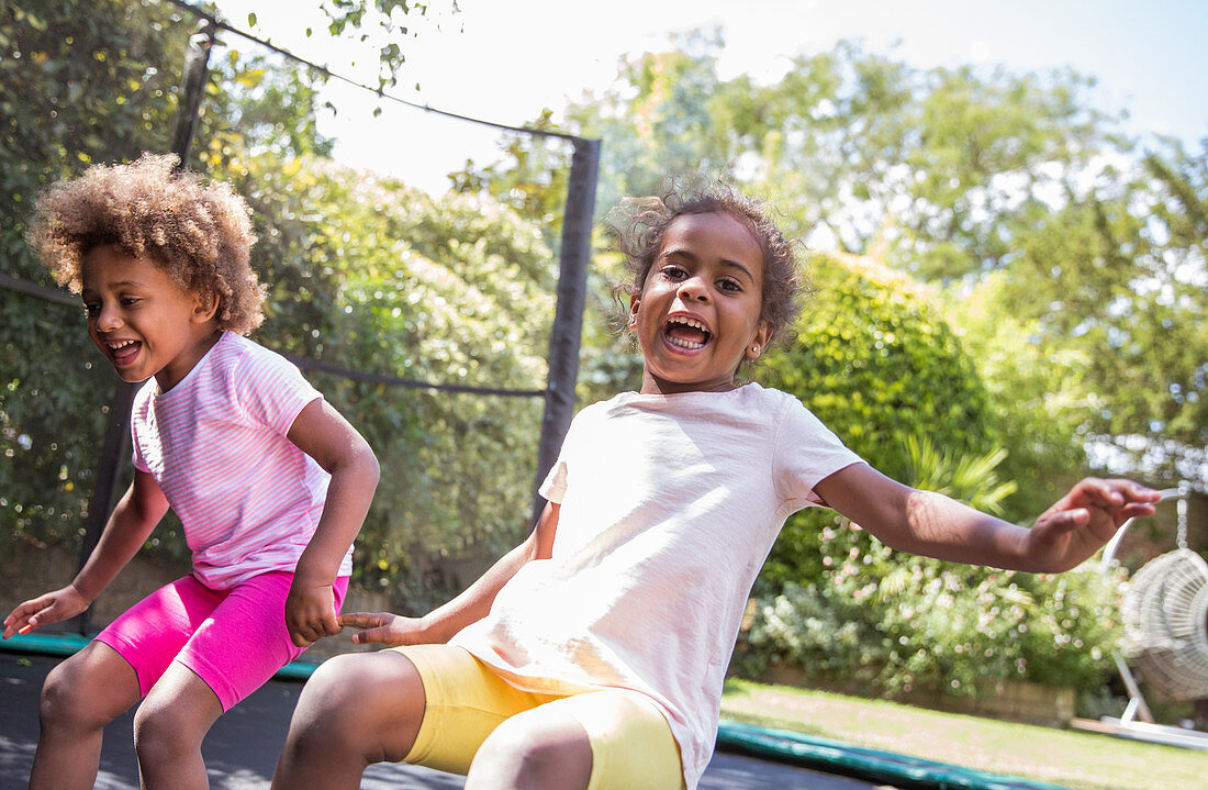 Portrait playful sisters jumping on backyard trampoline