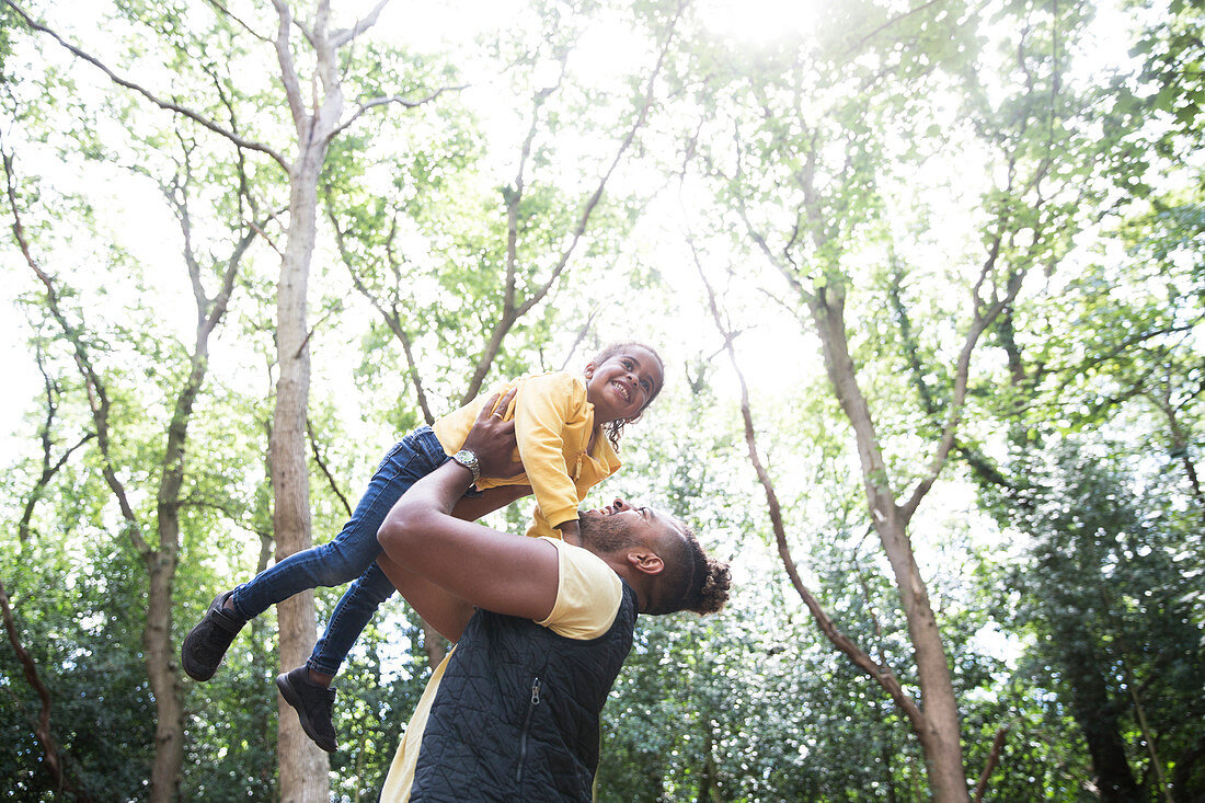 Playful father lifting daughter below trees in park