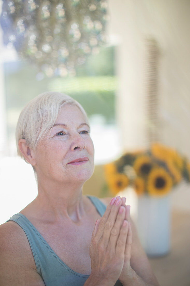 Serene senior woman meditating with hands clasped