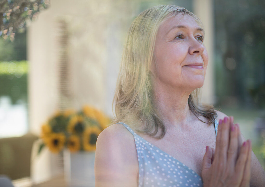 Serene senior woman meditating with hands clasped