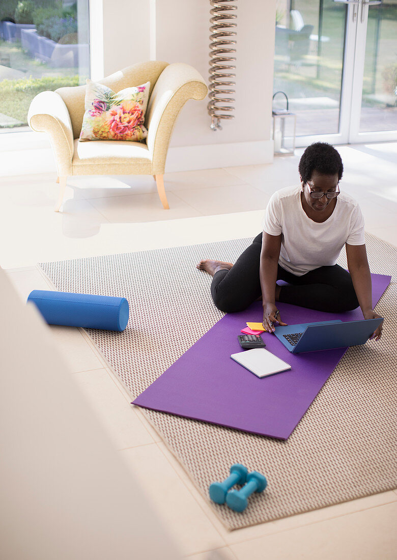 Mature woman working at laptop on yoga mat at home
