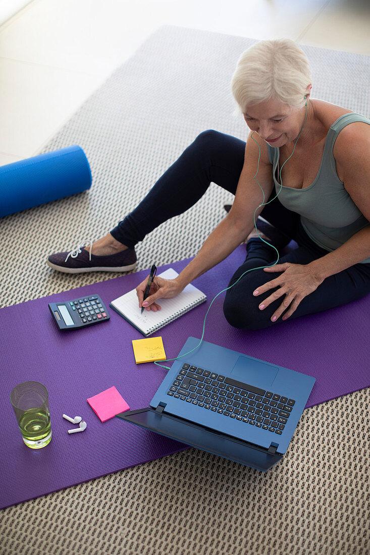 Senior woman working at laptop on yoga mat