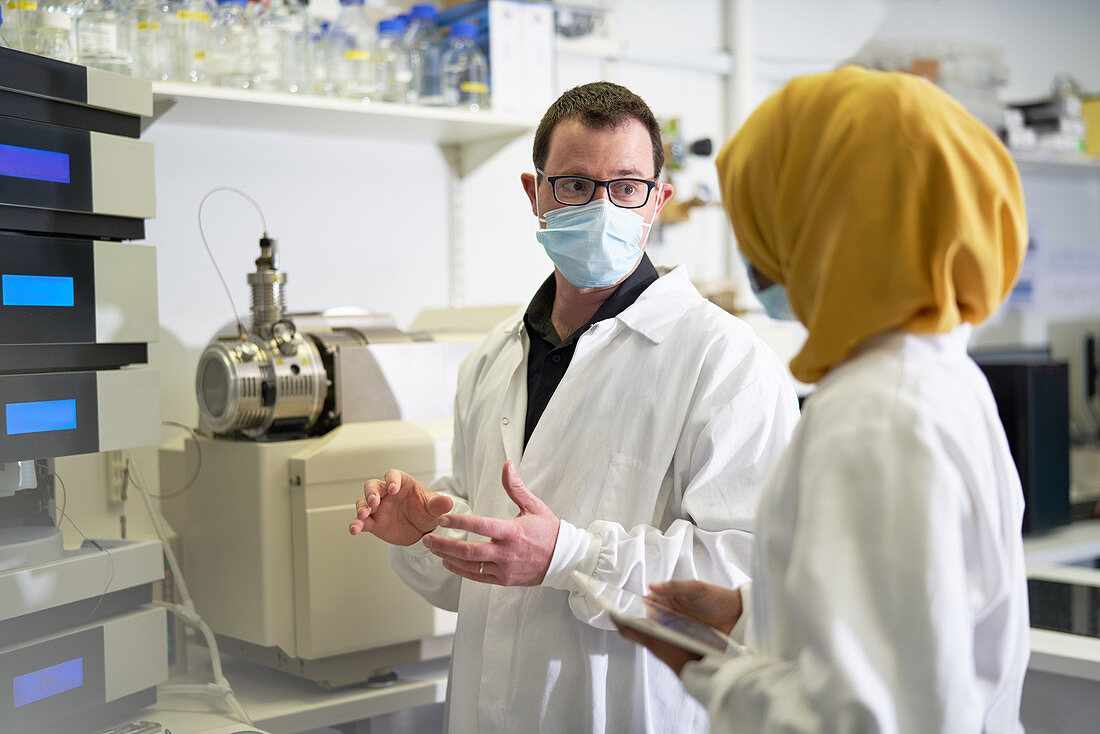 Scientists in face masks talking in laboratory