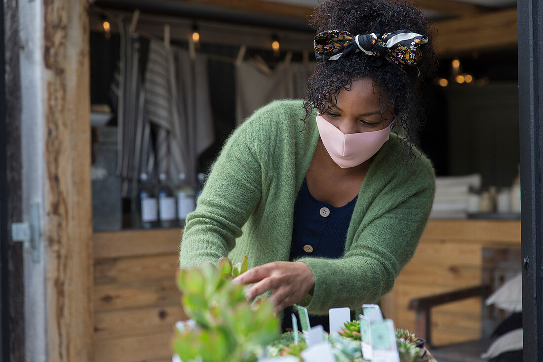 Female shop owner in face mask tending to plants