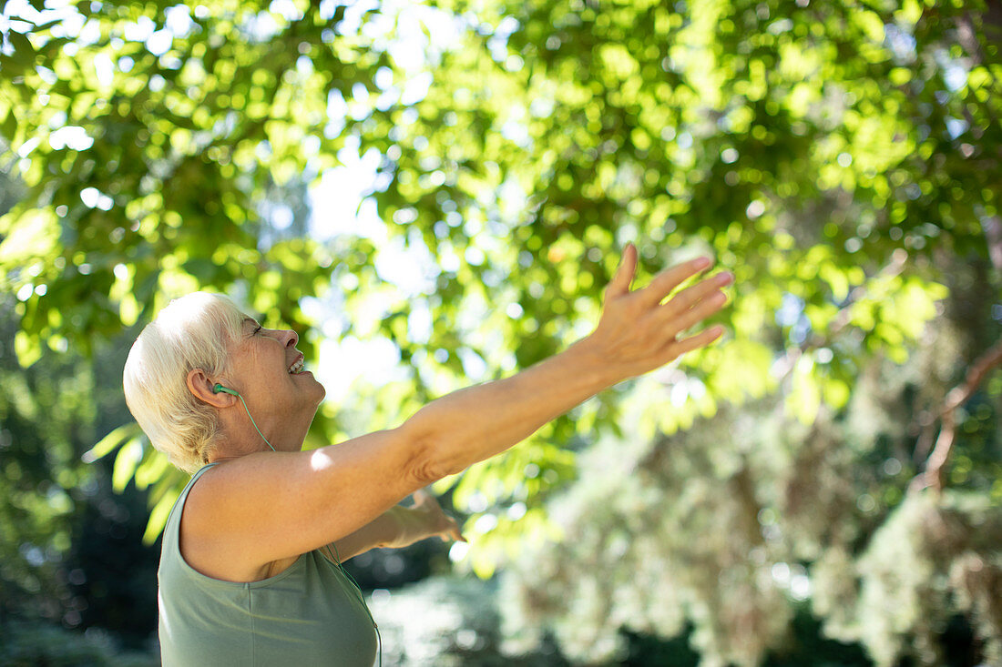 Senior woman with arms outstretched under summer trees