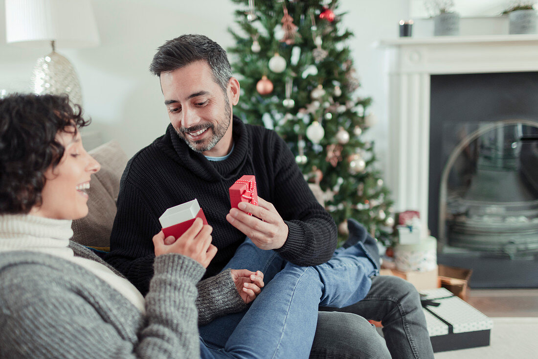Happy couple opening Christmas gift on living room sofa