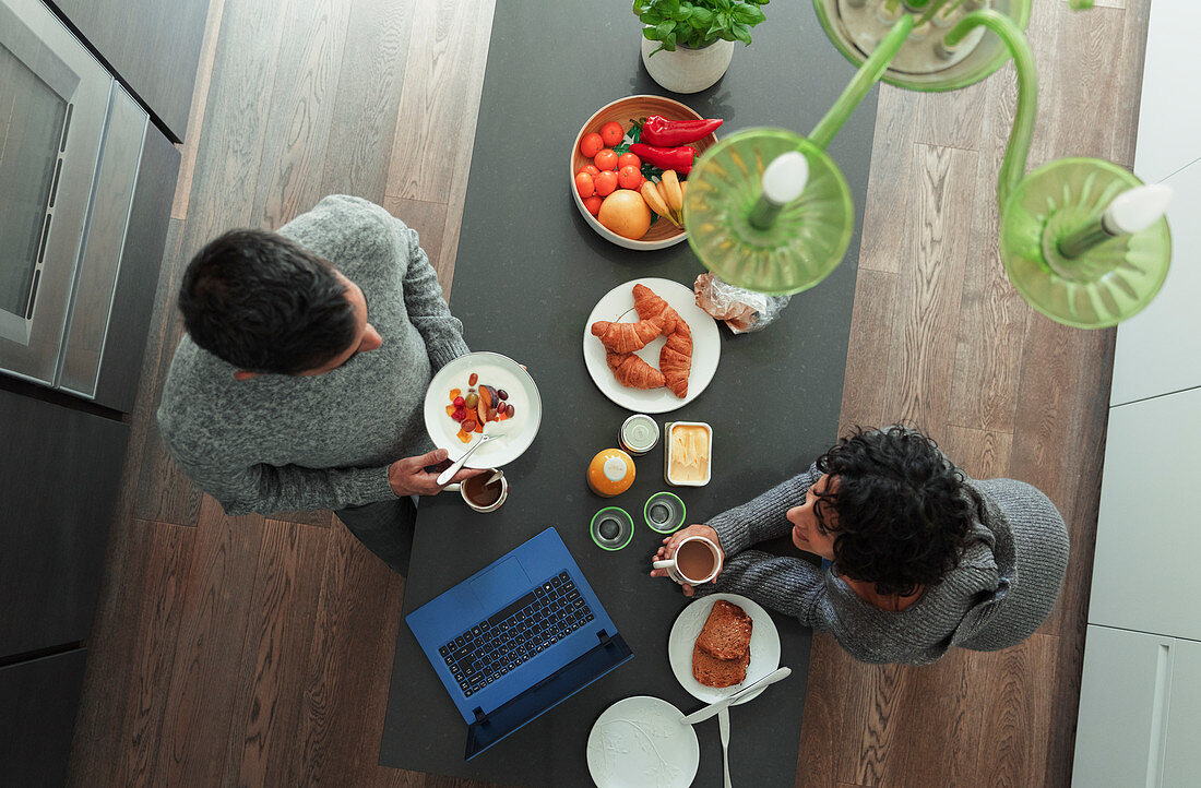 Couple enjoying breakfast at kitchen counter with laptop