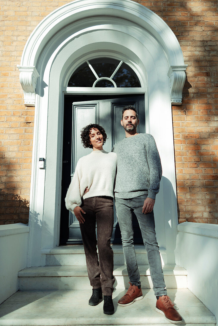 Portrait couple at arched front door on house stoop