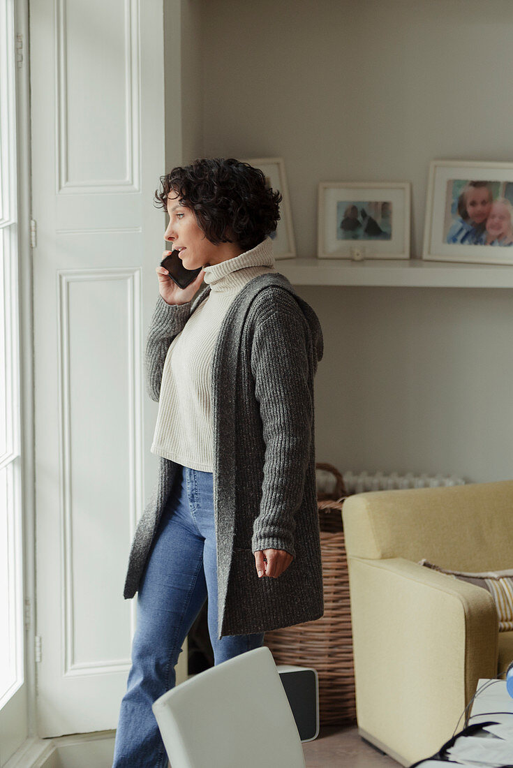 Woman talking on smart phone at living room window