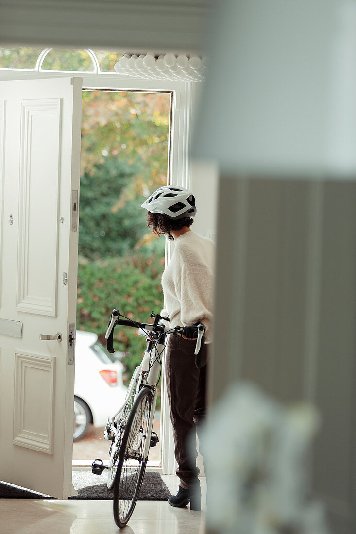 Woman with bicycle returning home through front door