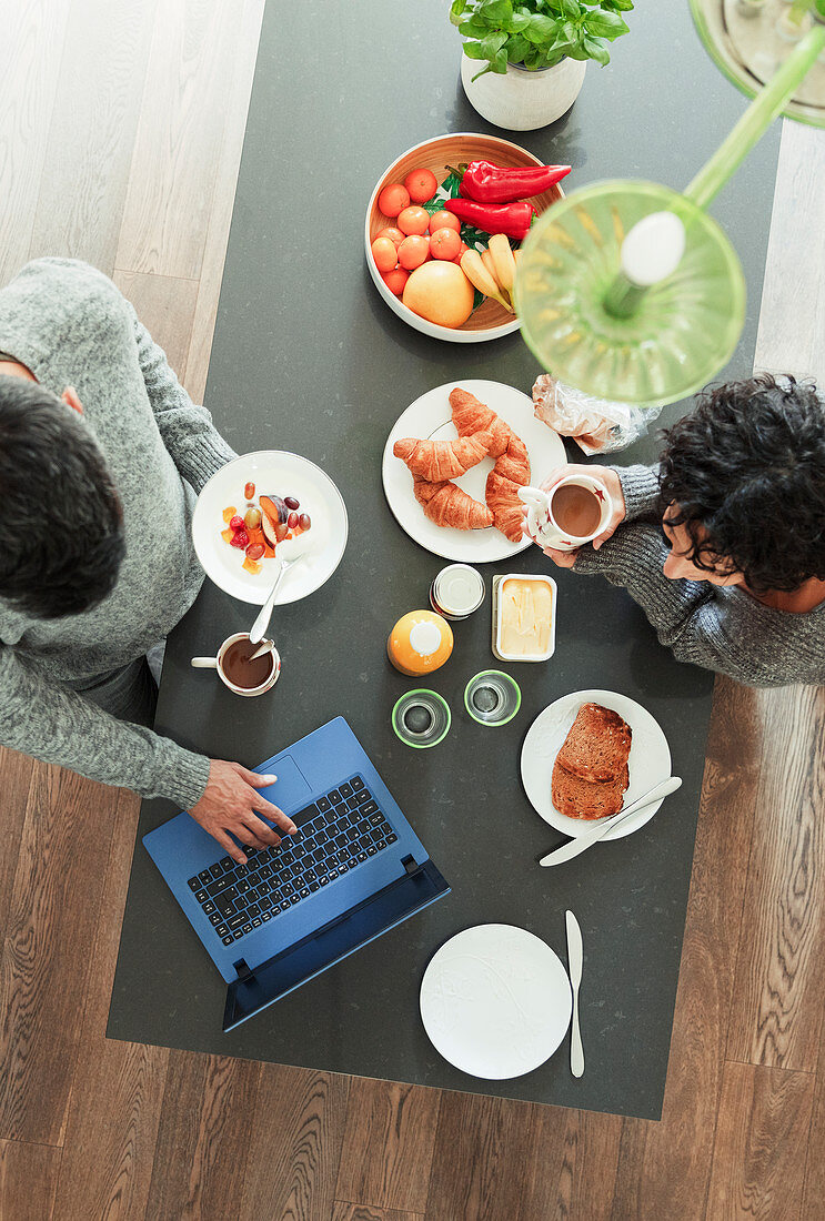 Couple enjoying breakfast and working at laptop