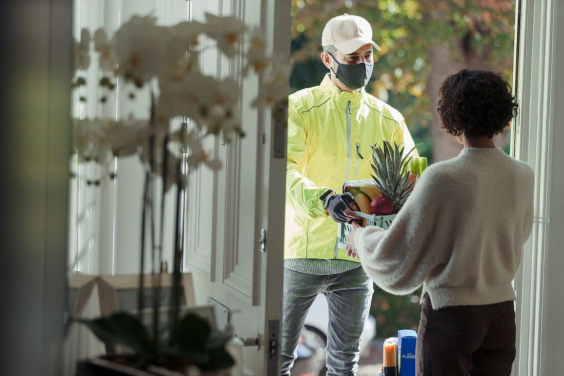 Woman receiving grocery delivery in face mask at door