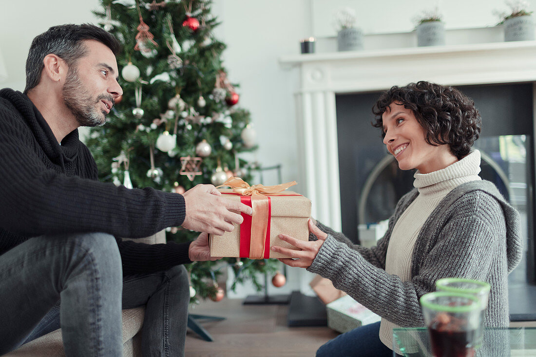 Husband giving Christmas gift to wife with tree