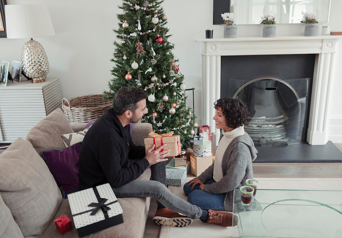 Husband giving Christmas gift to wife by tree