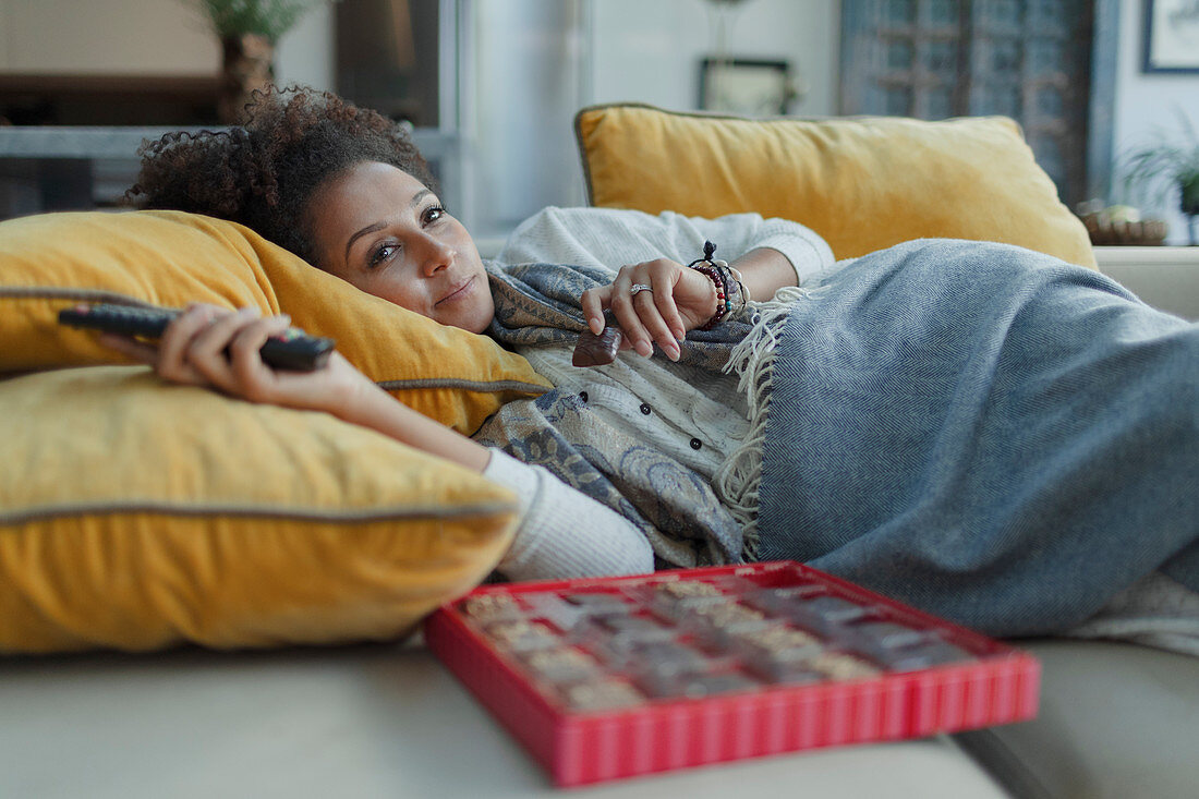 Cozy woman eating chocolates and watching TV