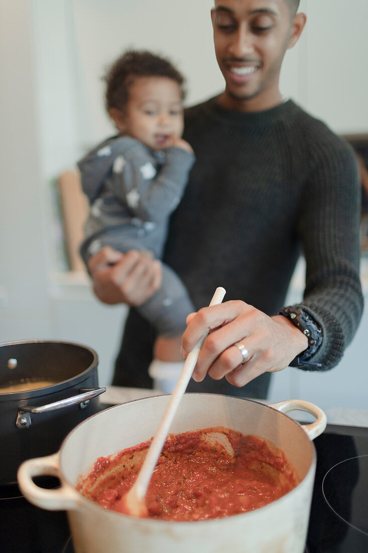 Father holding baby daughter and cooking spaghetti