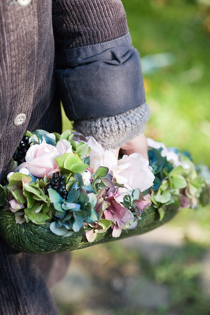 Arrangement of hydrangea blossoms, roses, privet berries, and snowberry in hollowed out zucchini