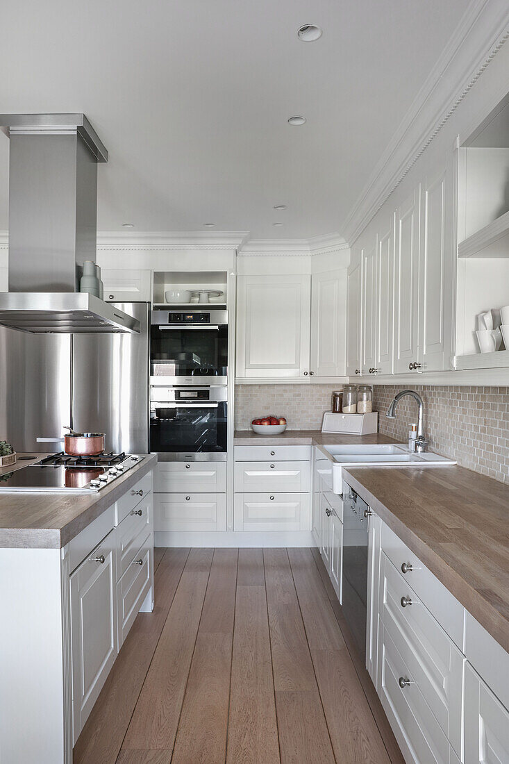 White fitted kitchen with extractor hood above hob on island counter