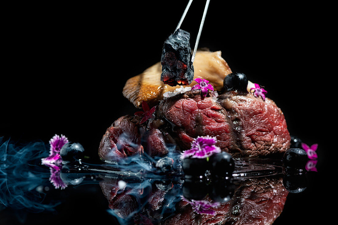 Flaming coal piece with tweezers on meat