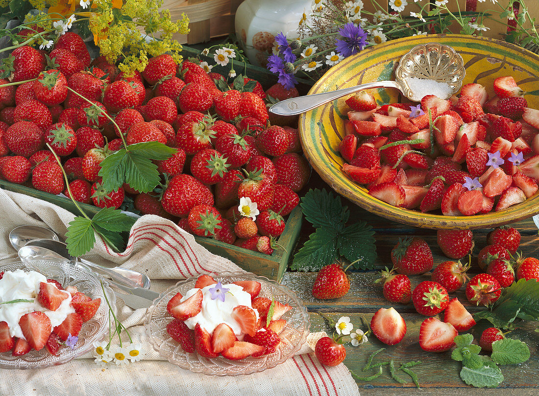 A bowl and a wooden box with strawberries, a plate with strawberries and cream