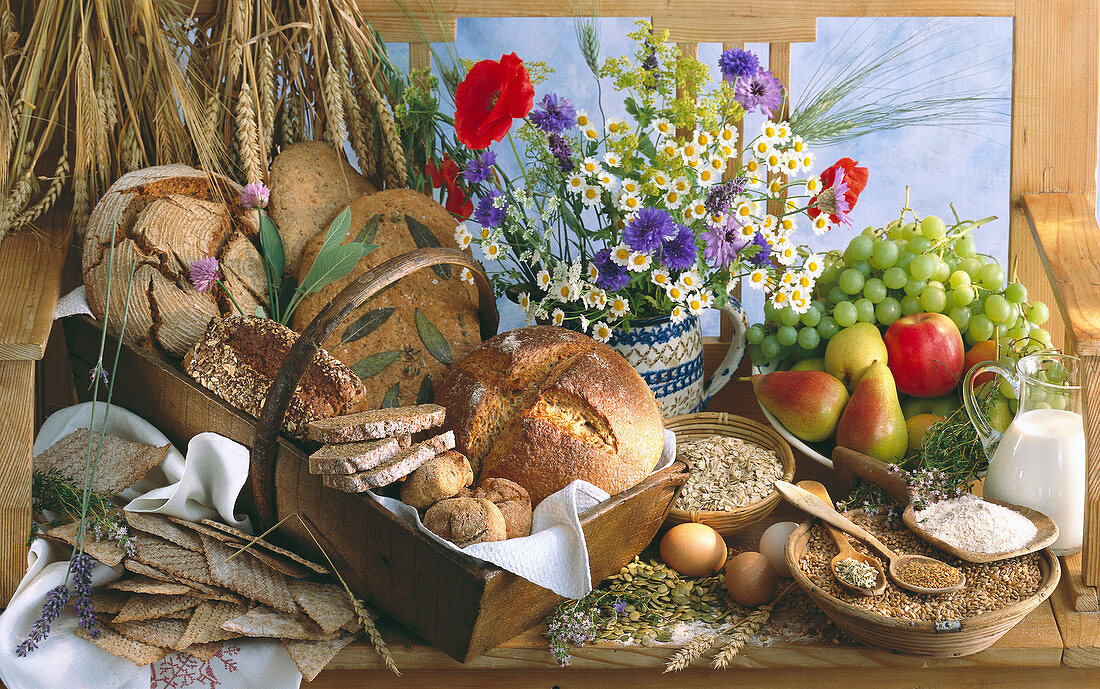 Stillleben mit Vollkornbrot, Getreide, Vollkornmehl, Sonnenblumenkernen, Haferflocken, Obst, Milch