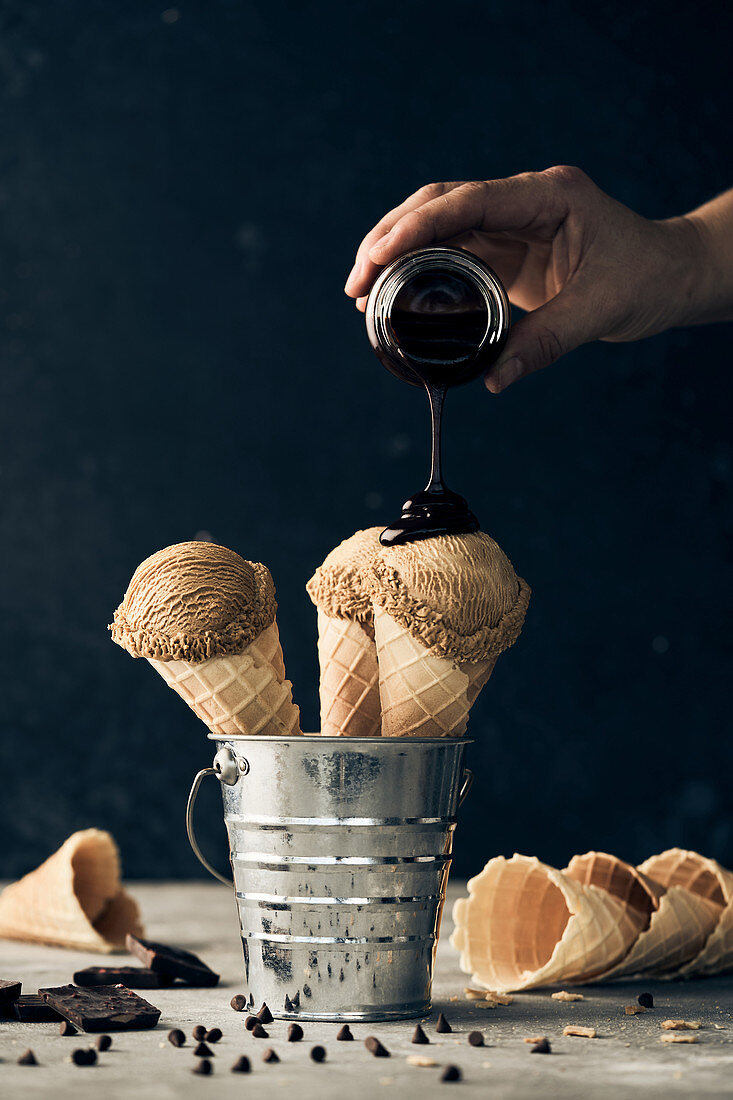 Adding chocolate topping on scoops of ice cream in waffle cones