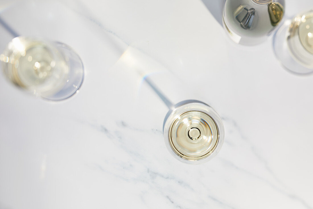 Three white wine glasses and a white wine bottle on a marble plate