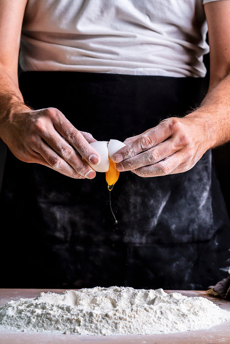 Breaking raw chicken egg into sifted flour pile