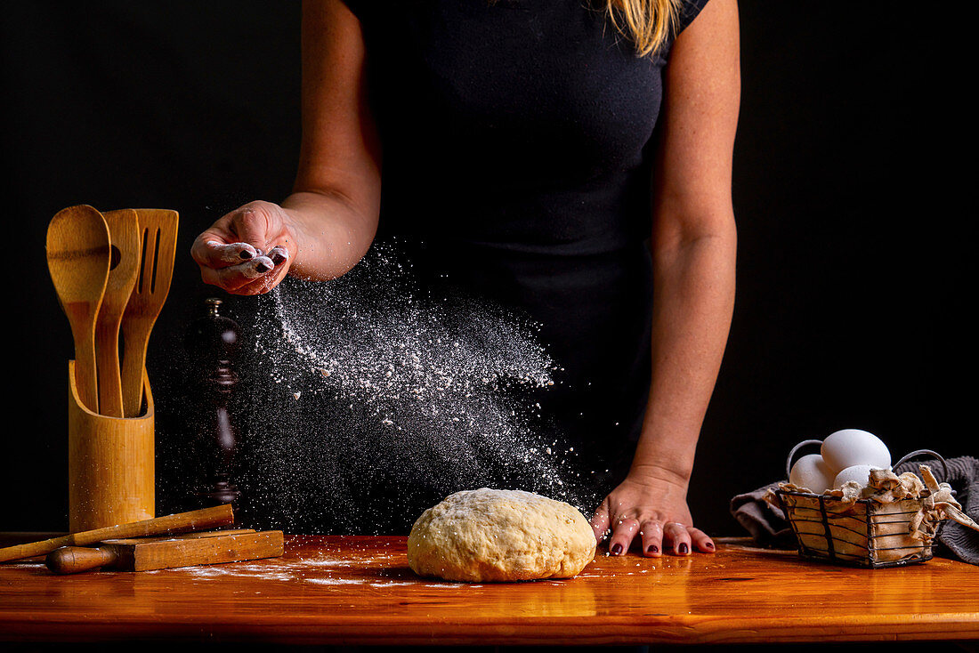 Female sprinkling kneaded bread dough with flour