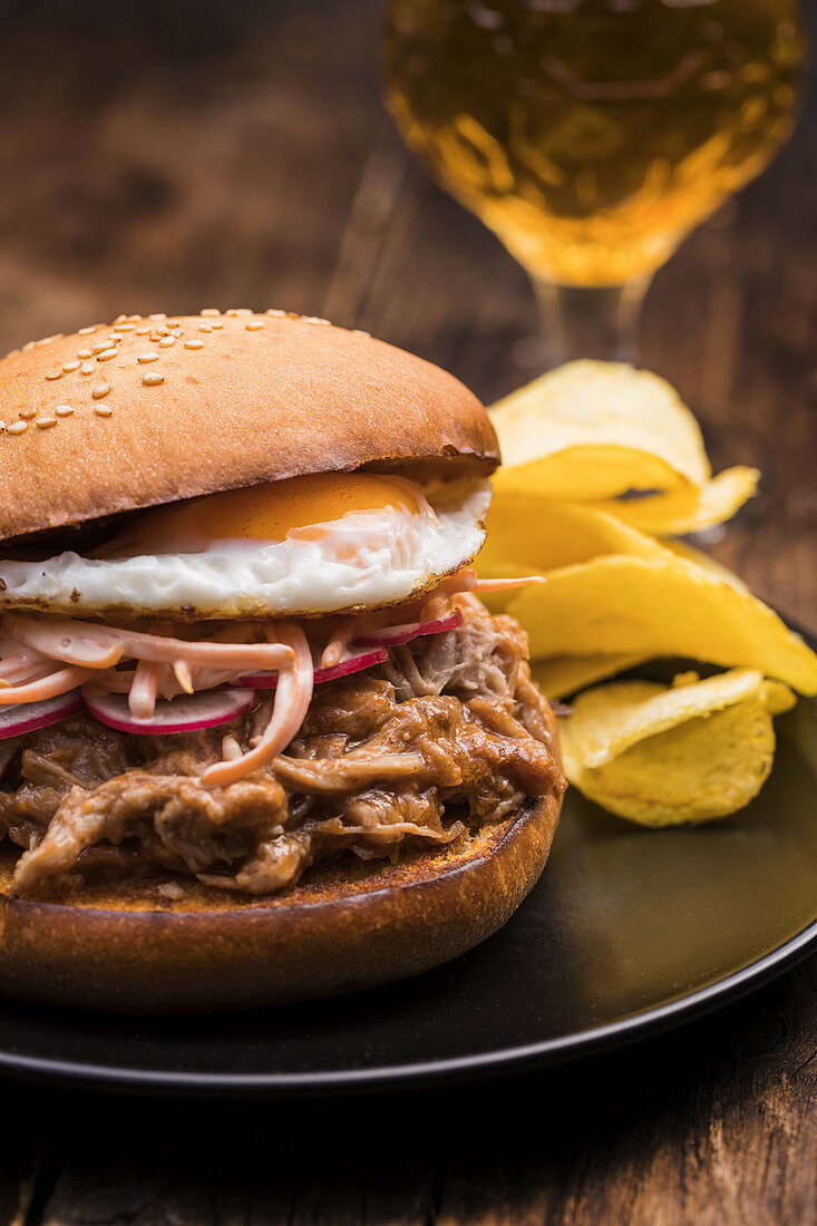 Pulled pork hamburger with vegetables, fried egg and potato chips