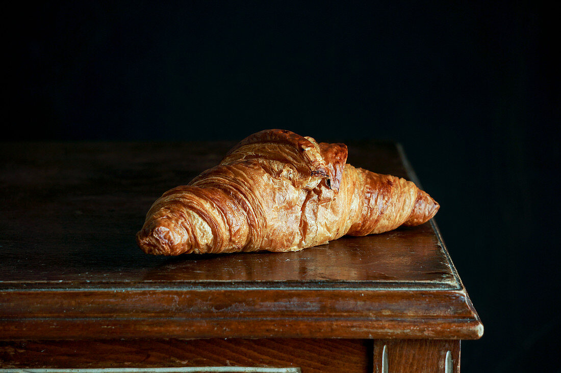 Ein Croissant auf Holztisch vor schwarzem Hintergrund