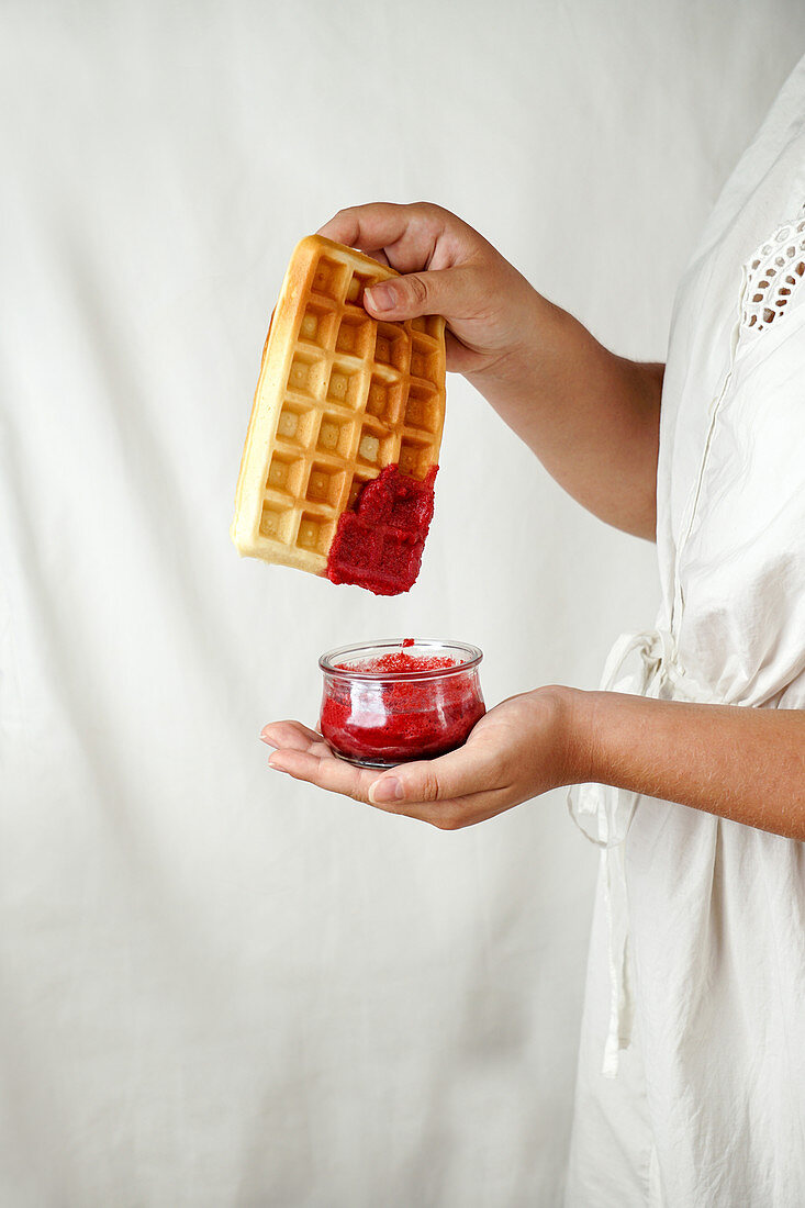 Woman holding waffle with red berry sauce