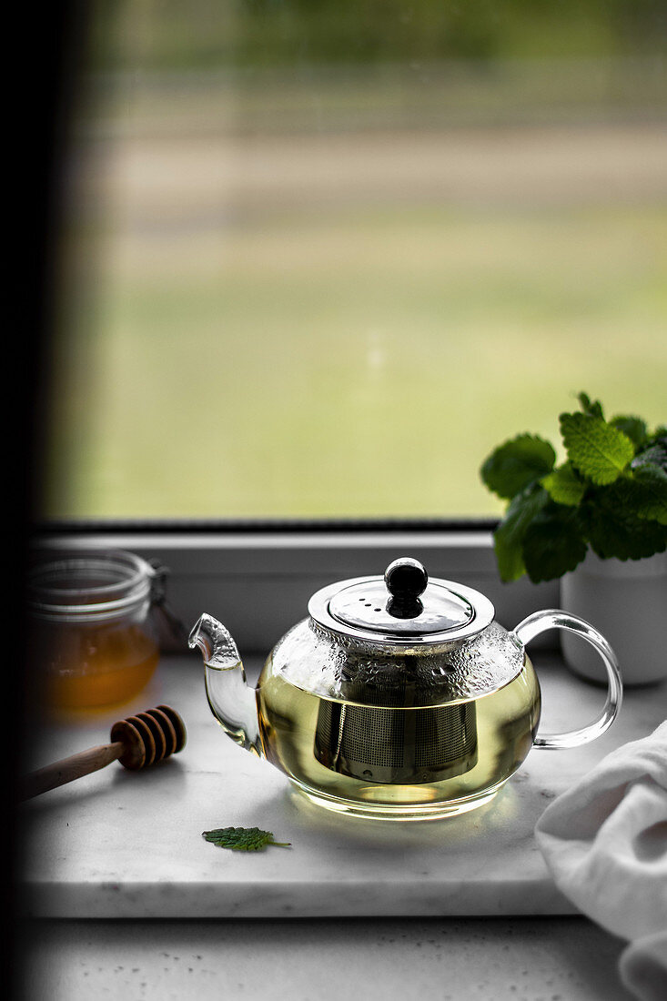 Mint tea in a glass teapot on a windowsill