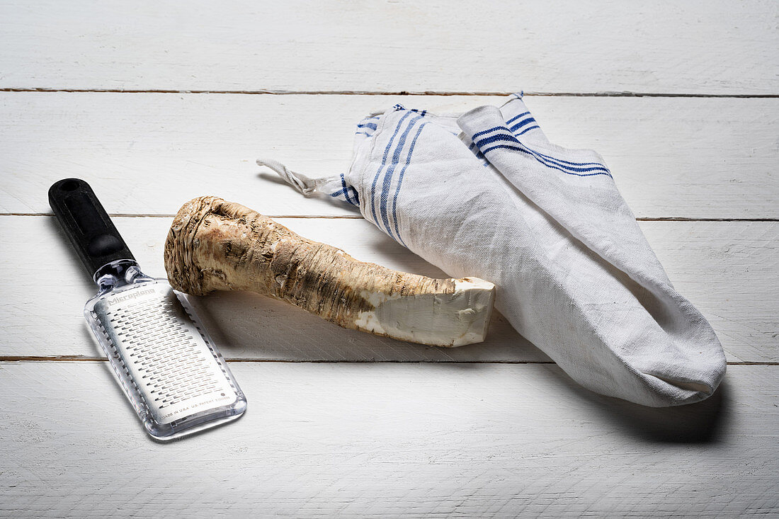 Horseradish root and grater on white wooden background