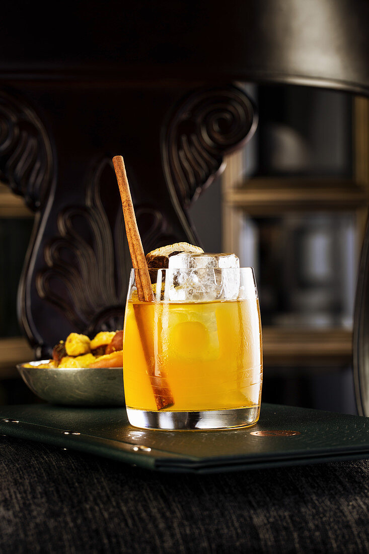 Gelber Cocktail im Glas mit Zimt und Orange