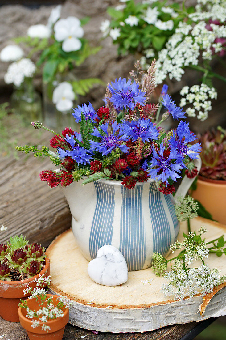 Kleiner Strauß aus Kornblumen und Inkarnatklee in Sahnekännchen auf Scheibe von Birkenholz, Herz aus Howlith